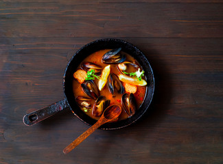 Mussels in red curry sauce on a wooden background.
