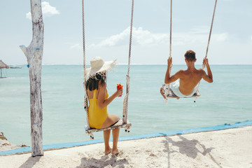 Teenage girl and boy hanging on swings with a sea view in beach cafe