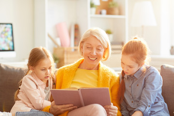 Portrait of smiling mature woman reading book o two little girls in sunlight, copy space