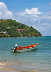 Fototapeta na wymiar A traditional fishing boat with an outboard motor is anchored in the bay of a fishing village in a Caribbean island