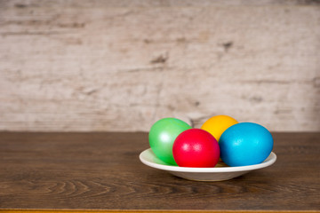 Fototapeta na wymiar red, yellow, green and blue easter eggs in plate on wooden table