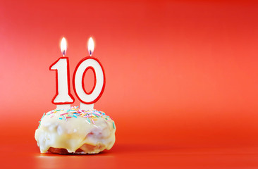 Ten years birthday. Cupcake with white burning candle in the form of number 10. Vivid red...