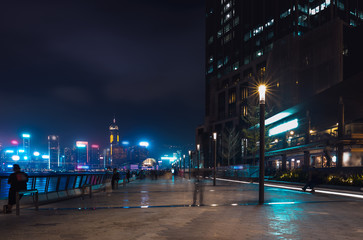 Hong Kong cityscape at night. Tourists walking on the waterfront