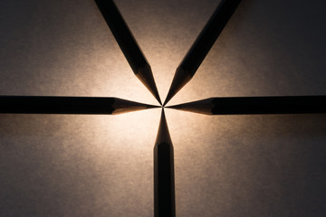 Silhouette of pencils, photographed over a piece of paper with a source of light under it.