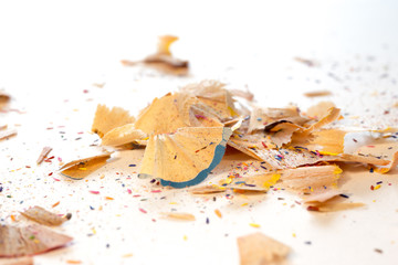 Chippings of color pencils of different colors, scattered over a piece of paper sheet.