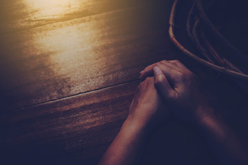 close up of woman hands prays near crown of throne on wooden table with sunlight from window,...
