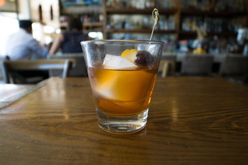 cocktail with orange and cherry garnish on a wooden table with couple in the background