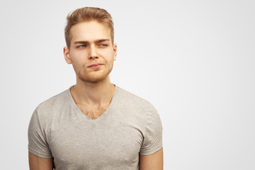Fototapeta premium Puzzled man keeps lips pressed, has frustrated facial expression, frowns face in displeasure, being deep in thoughts. Male dressed in casual outfit, models over white wall with copy space