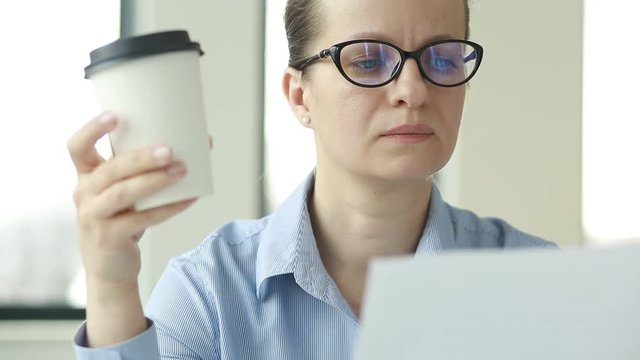 Businesswoman in her office drinking coffee.Portrait of calm pleased woman in eyeglasses holding cup with hot beverage in hands.  