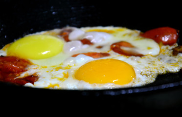 Fried eggs with colorful yolks and tomatoes. Fried on a black cast iron skillet.