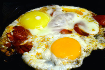 Fried eggs with colorful yolks and tomatoes. Fried on a black cast iron skillet.