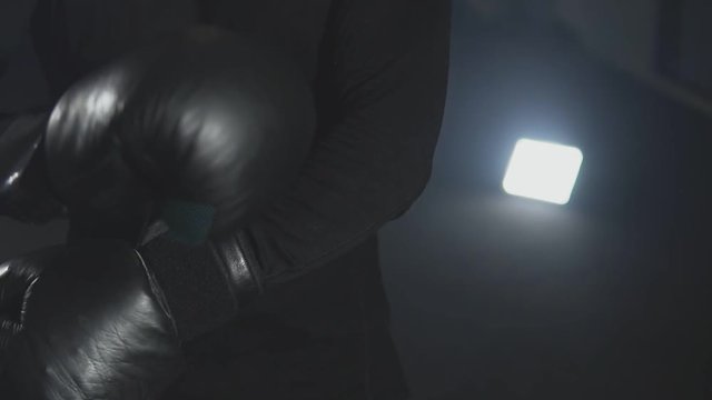 Close-up of kickboxer wearing boxing gloves against black background in slow motion. Boxer prepare for training.
