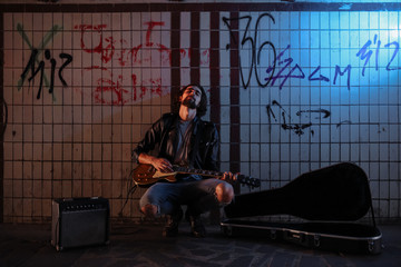 A street musician playing on guitar in the underpass. Vagrant lifestyle. Playing in the underpass to make a living. Unemployed musician. Future rock star.