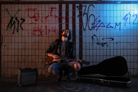 A street musician playing on guitar in the underpass. Vagrant lifestyle. Playing in the underpass to make a living. Unemployed musician. Future rock star.