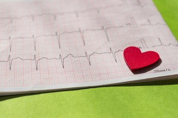 close up of an electrocardiogram in paper form vith red wooden heart. ECG or EKG paper on green ...