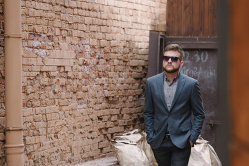 A man with a beard and sunglasses in a gray suit poses on the street to advertise men's clothing. Advertising menswear