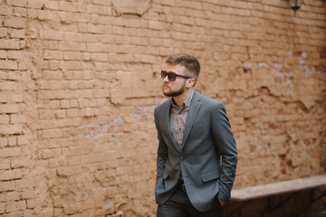 A man with a beard and sunglasses in a gray suit poses on the street to advertise men's clothing. Advertising menswear
