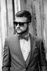 A man with a beard and sunglasses in a gray suit poses on the street to advertise men's clothing. Advertising menswear