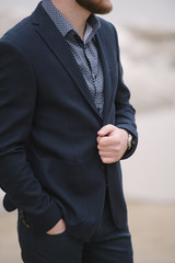 A man with a beard in a blue suit poses on the street to advertise men's clothing. Advertising menswear