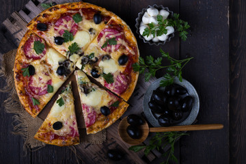 Fototapeta na wymiar Pizza served with dill. Pizza with tomatoes black olives and ham.