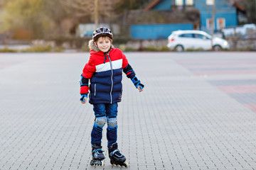 Cute school kid boy skating with rollers in the city. Happy healthy child in protection safety...