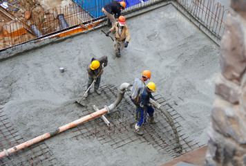 Five workers poured cement construction. Two of them hold a pipe from which cement flows.