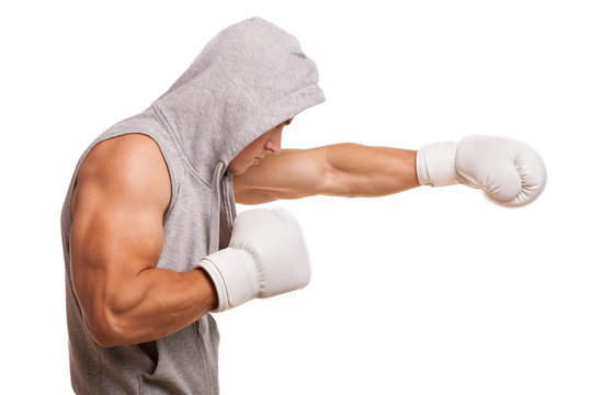 Profile shot of a male boxer shadow boxing isolated on white. Ripped muscular fighter wearing hoodie, exercising before fight, copy space. Professional muay thai boxer working out. Power, strength