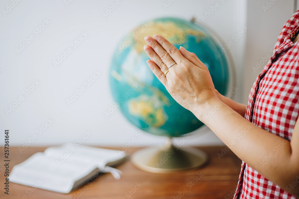 Wall mural close up of woman hands praying over blurred world globe and bible on wooden table with white wall b