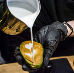 The barista in black gloves prepares a cappuccino with latte an art in avocado. Unusual cup. Fresh and beautiful coffee with milk.
