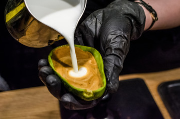 The barista in black gloves prepares a cappuccino with latte an art in avocado. Unusual cup. Fresh and beautiful coffee with milk.