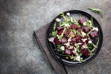 beetroot salad with blue cheese, arugula and walnut in a black plate on stone background, top view