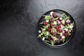 beetroot salad with blue cheese, arugula and walnut in a black plate on stone background, top view