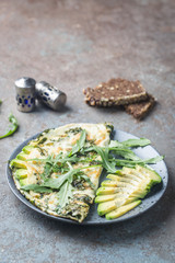 Omelette with avocado and arugula on gray ceramic plate on stone background, top view. Healthy breakfast.