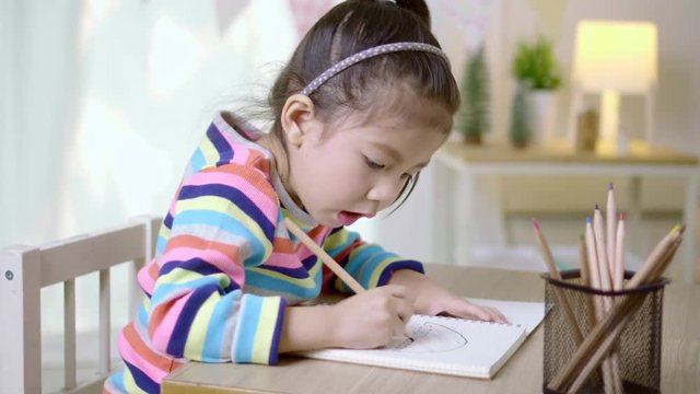 Close up shot asian little girl writing and drawing a notebook on the wooden table at home, Educational concept for school
