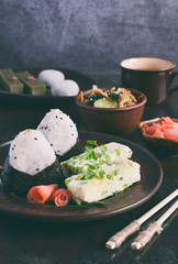 Mix of Japanese food - rice balls onigiri, omelette, ginger, sunomono wakame cucumber salad. Traditional dessert of bean and green tea matcha - jelly yokan, daifuku mochi. Asian breakfast or lunch