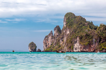 Naklejka premium People on the longtail motor boat sailing to water caves. Mountain, and Phi Phi islands on background. View from water line. Blue sky, sunny day