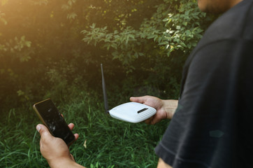 Man is looking for wi-fi signal in the nature. Guy is lost and holding router with smartphone  in...