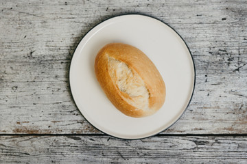Top view of German or Austrian style bread roll or bun, a small loaf made of wheat flour and sourdough traditionally served for breakfast on white plate and wooden background