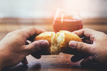 Man hand holding bread with a cup of wine  on wooden table for communion, Christian background with copy space