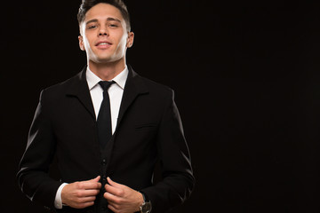 Portrait of a handsome young man wearing elegant black suit and tie posing confidently on black...