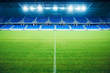 Modern Football Stadium in the evening. Soccer arena, background. Green grass, blue seats