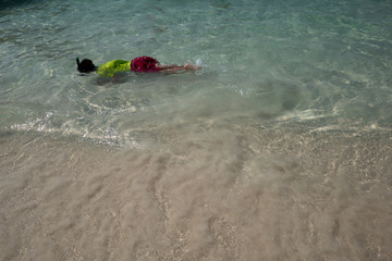 boy in bright green shirt and red pants is having fun with snorkeling at shallow clear sea near the...