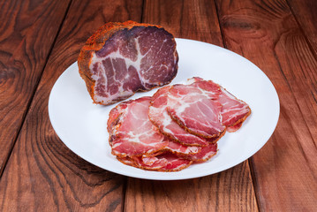 Partly sliced dried pork neck on dish on rustic table