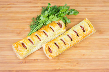 Two baked sausage rolls with herbs on wooden bamboo surface