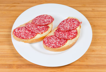 Open sandwiches with salami on dish on a wooden surface