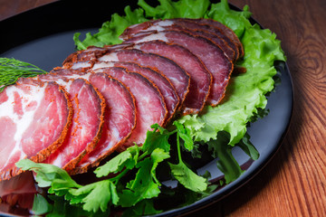 Sliced dried pork neck with greens on black dish closeup