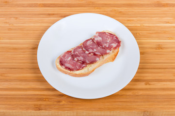 Open sandwich with dry-cured sausage on white dish