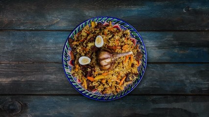 Pilaf on plate with oriental ornament. Central-Asian cuisine - Plov. Rotates on wooden background. Top view