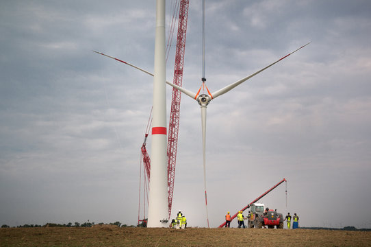 A construction crane lifts all three rotor blades of a wind turbine