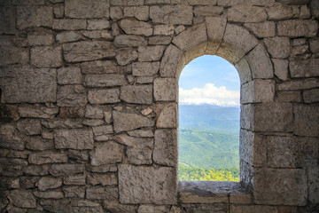 Stone war tower window with motion blurred bird and sea coast view with green tree hills - Powered by Adobe